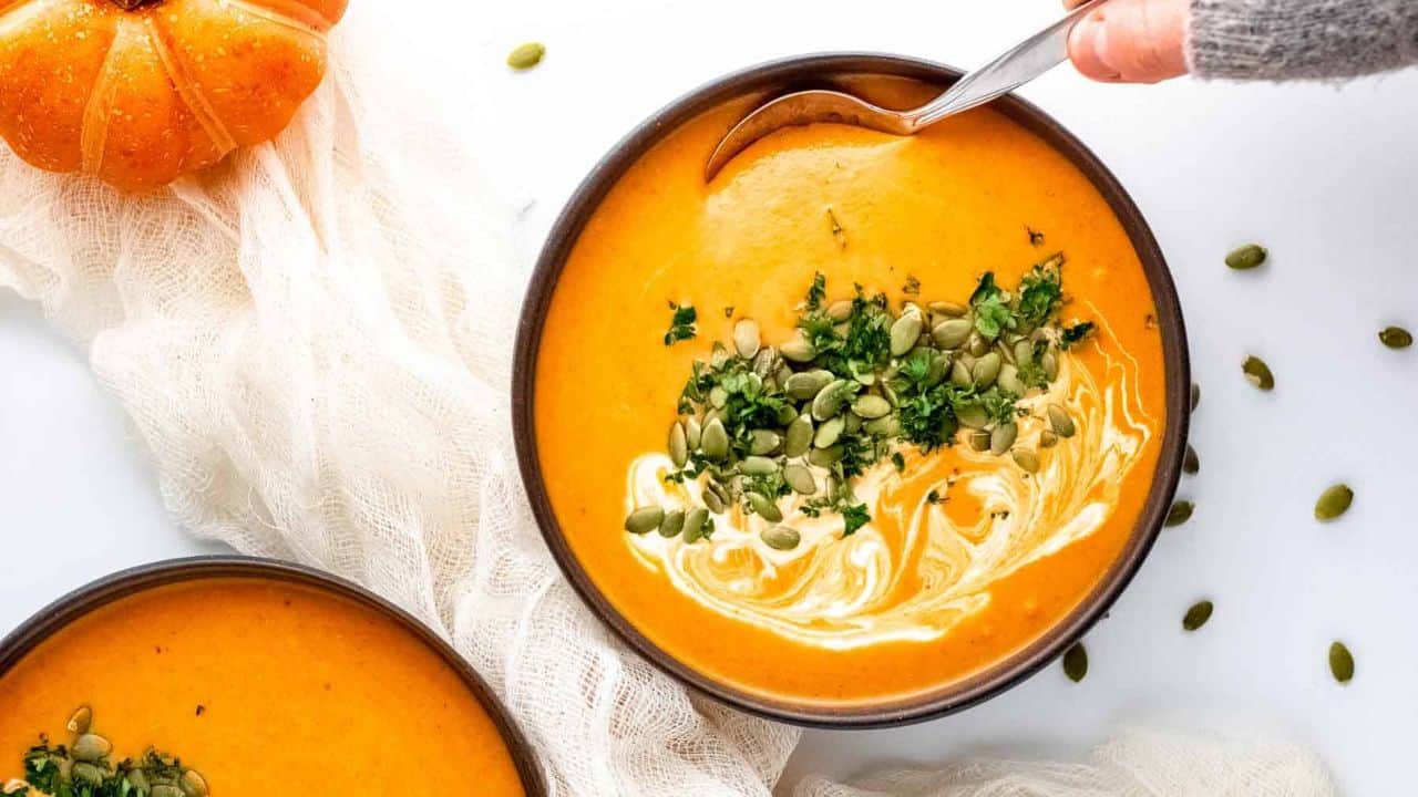 Two bowls of curry pumpkin soup with coconut cream and pumpkin seeds.
