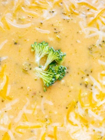Close-up of creamy broccoli cheese soup with shredded cheese on top and a small broccoli floret in the center.