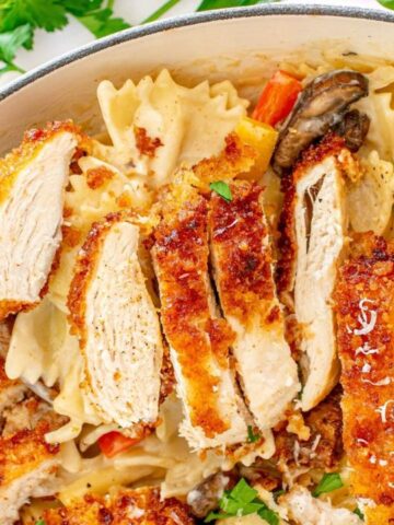 Pan of pasta and vegetables topped with crispy slices of breaded chicken.