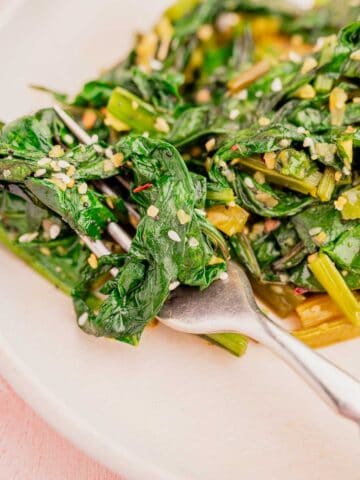 A plate of sautéed greens with sesame seeds and a fork.