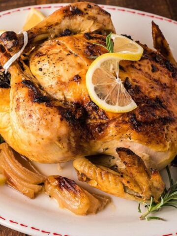 Roasted chicken garnished with lemon slices and rosemary on a white platter.