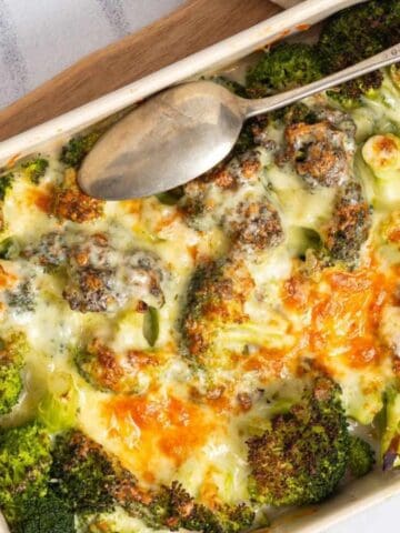A baked broccoli and cheese casserole in a rectangular dish, topped with melted cheese, with a serving spoon resting on top.