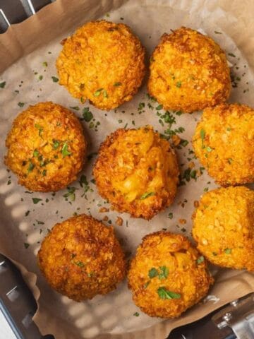 Seven golden-brown croquettes on parchment paper in an air fryer basket, garnished with chopped herbs. Lime wedge and sauce on the side.