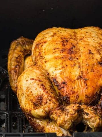 A whole roasted chicken with a golden-brown crust placed inside an air fryer basket.