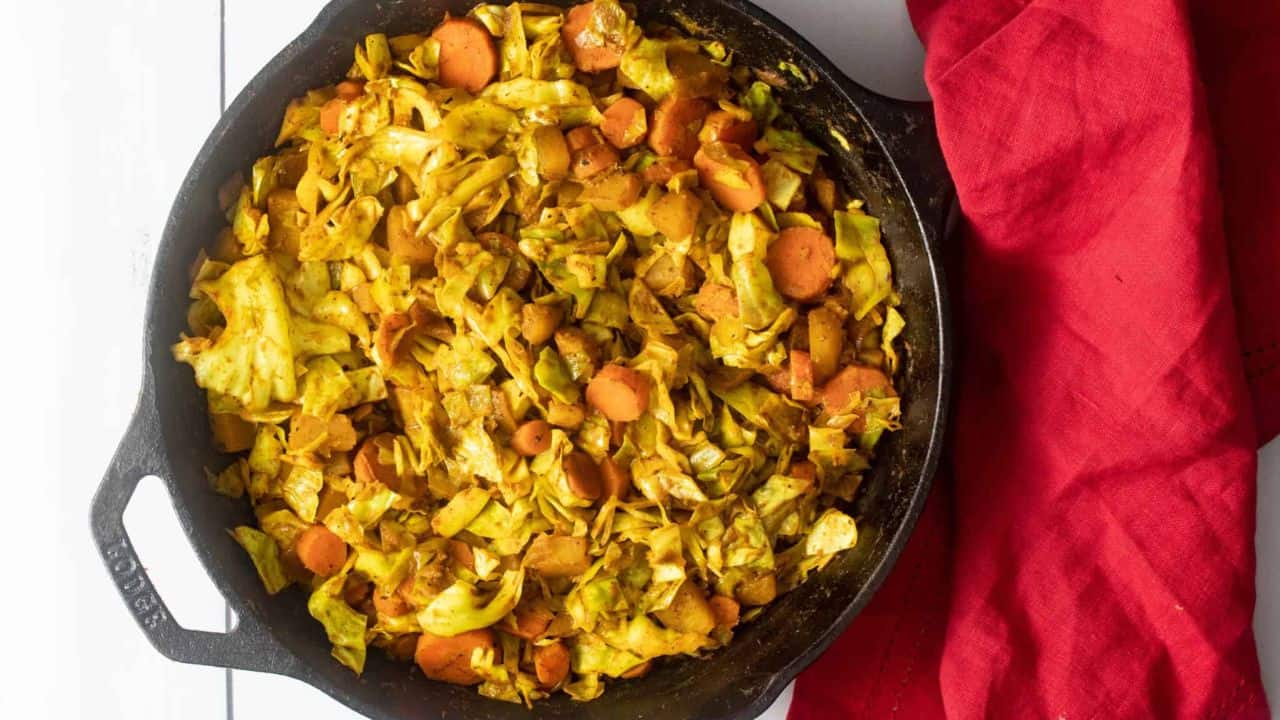 A close up image of cooked Ethiopian cabbage in a skillet pan with a wooden serving spoon mixing the dish.