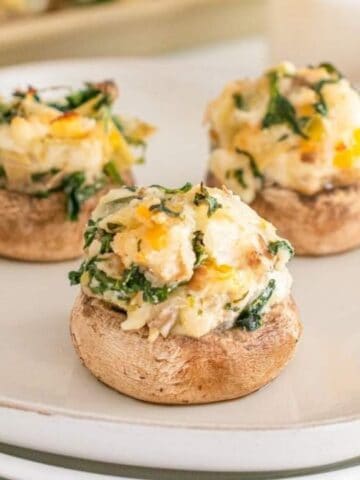 Three stuffed mushrooms with spinach and cheese filling on a white plate.