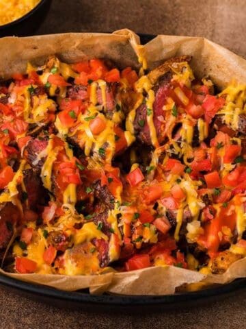 A dish of roasted potato skins topped with melted cheese, diced tomatoes, and herbs, served in a black baking dish.