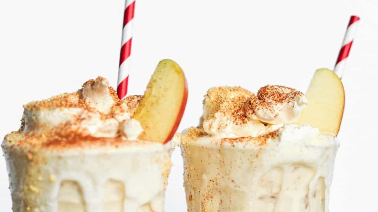Apple pie milkshake with a straw and apple slices.