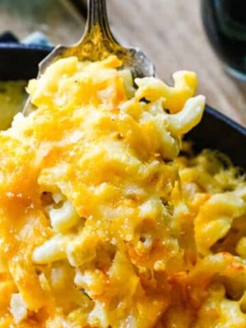 A close-up of a fork lifting a portion of baked macaroni and cheese from a black pan.