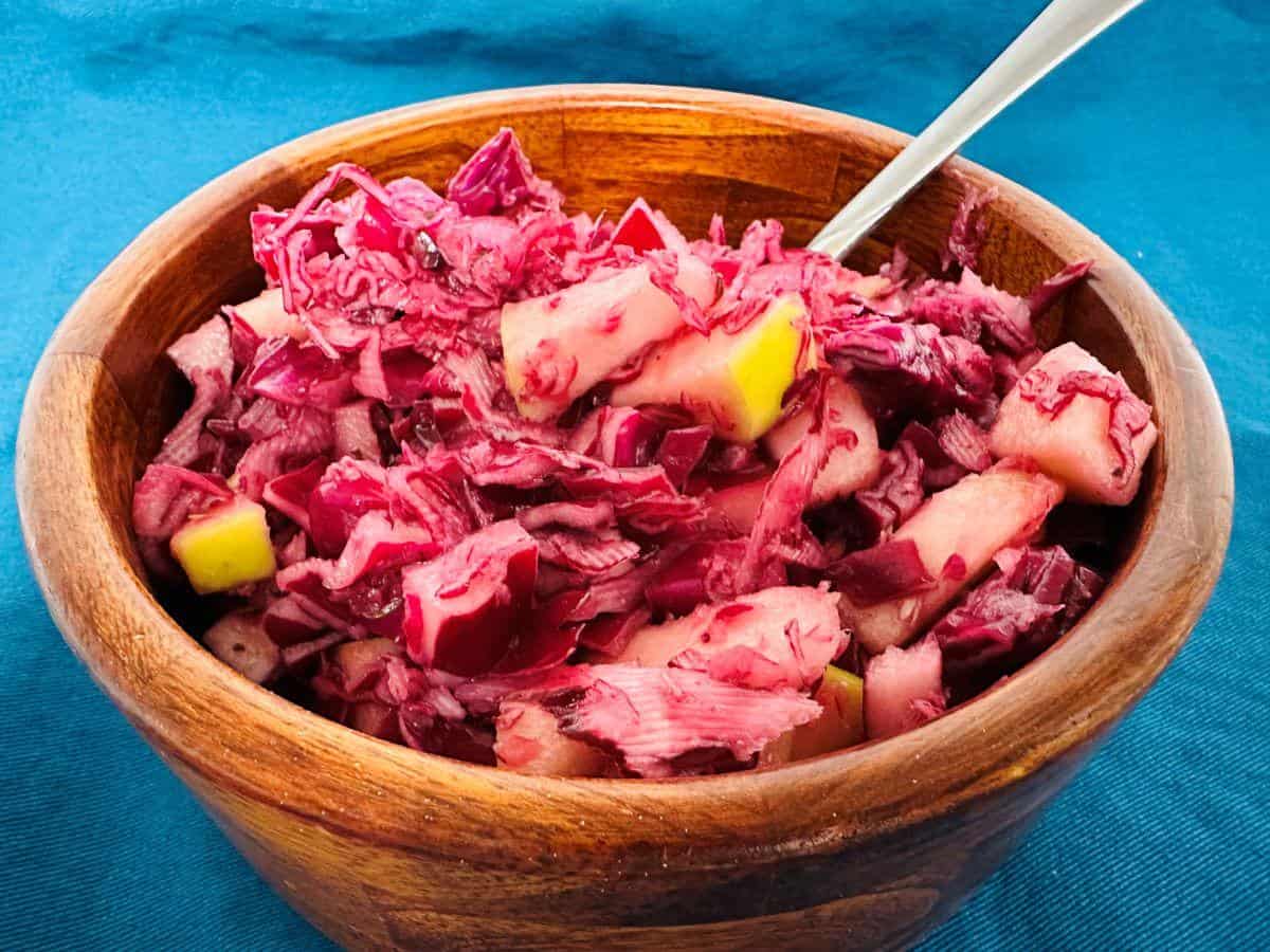 Red cabbage slaw in a wooden bowl with a spoon.