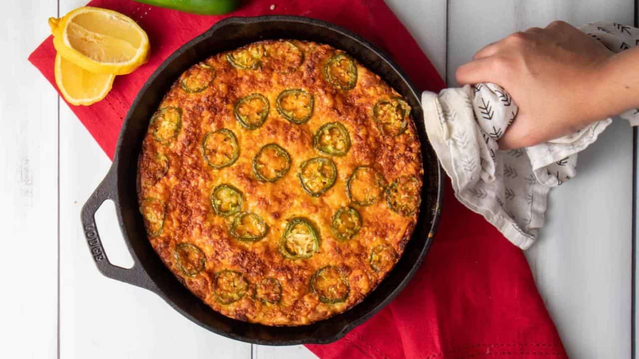 An overhead image of a hand holding a cast iron skillet with cornbread.