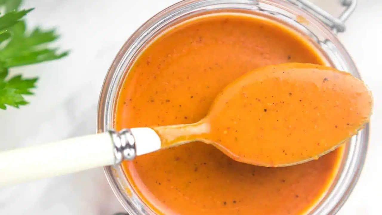 Enchilada Sauce in a glass container with a spoon on top.