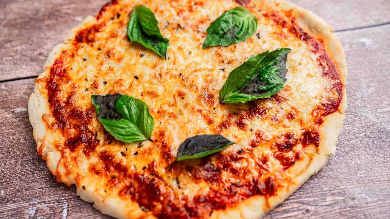 A cheese pizza on a wooden surface, topped with fresh basil leaves.