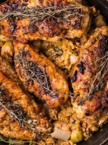A cast iron pot filled with roasted chicken breasts seasoned with herbs, placed on a bed of rice and vegetables on a wooden surface.