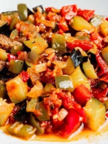 A white plate with ratatouille, featuring diced zucchini, bell peppers, and tomatoes, served with two slices of whole grain bread.