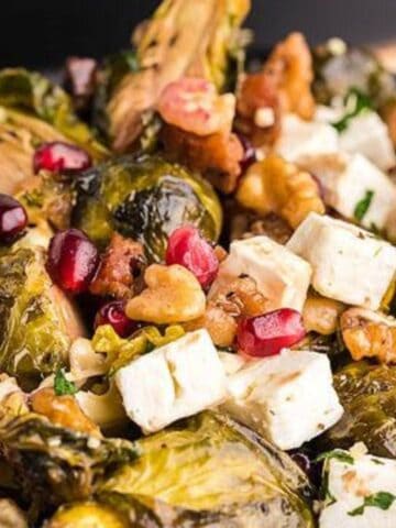 A plate of roasted Brussels sprouts with feta cheese, walnuts, and pomegranate seeds.