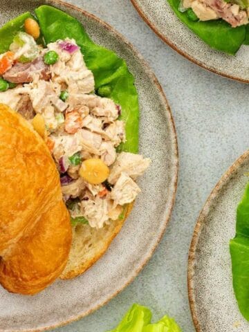 Croissant sandwiches with chicken salad on plates, garnished with lettuce. Grapes on the side.