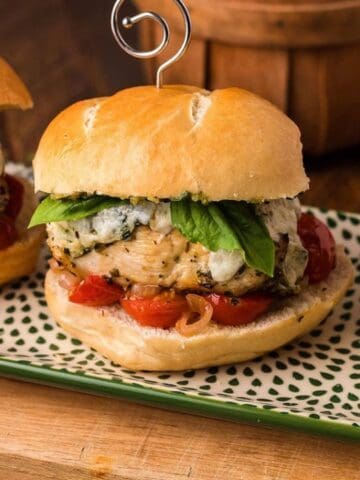 Three chicken sliders on a rectangular plate, each topped with mozzarella, basil, and tomato slices on a wooden board.