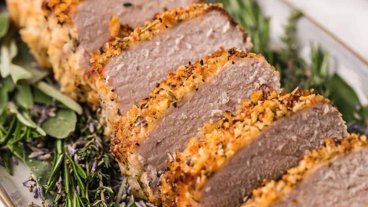 Sliced herb-crusted meat on a platter with fresh rosemary and other herbs.