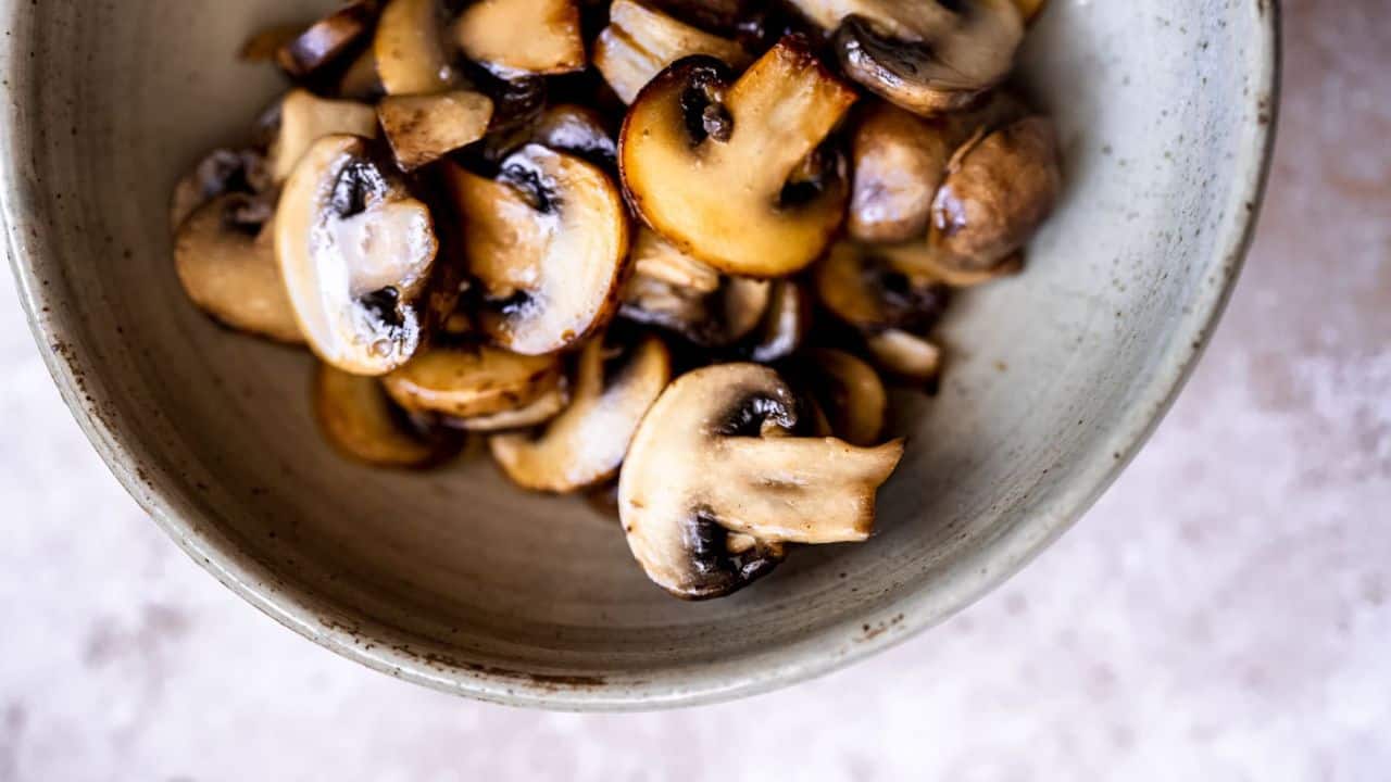 A bowl filled with sliced, cooked mushrooms on a light-colored surface.