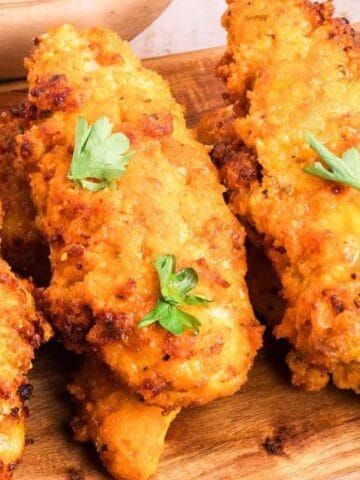 Crispy golden-brown chicken tenders are arranged on a wooden board, each garnished with a small sprig of fresh parsley.