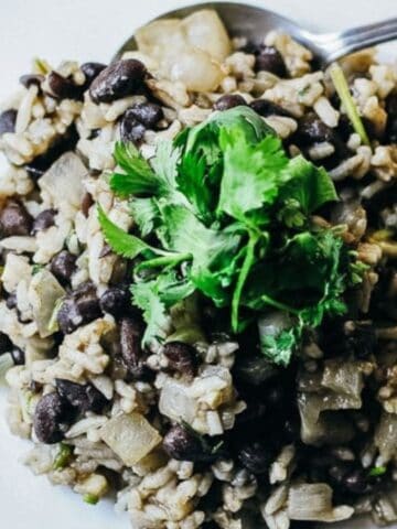 A plate of black beans and rice garnished with fresh cilantro, served with a spoon on a white dish.