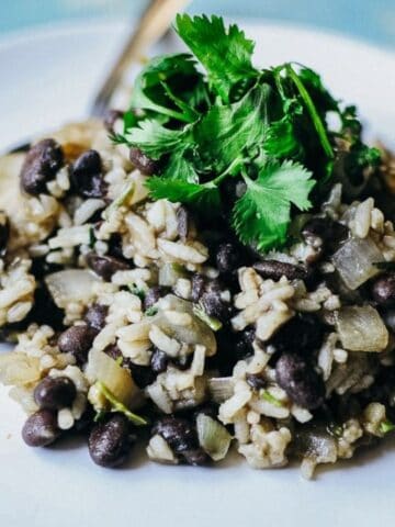 A serving of rice and black beans garnished with fresh cilantro is presented on a white plate with a spoon.