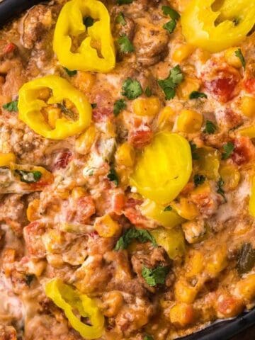 A black dish filled with a creamy casserole featuring corn, diced vegetables, and sliced yellow peppers on top.