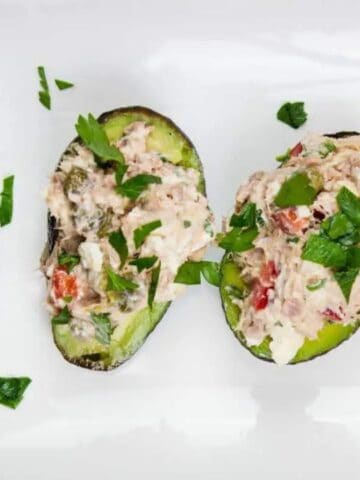 Four avocado halves filled with tuna salad, garnished with chopped parsley, arranged on a white rectangular plate.