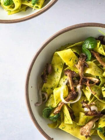 Two bowls of pasta with mushrooms and greens, accompanied by a striped cloth on the side.