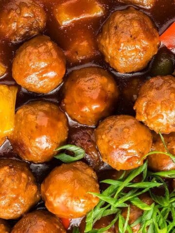 A pan of meatballs in rich sauce, garnished with chopped green herbs.
