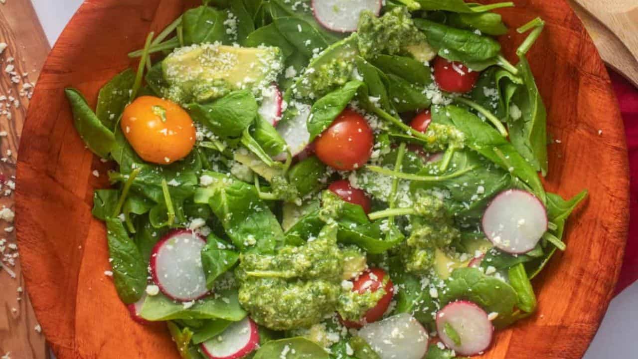 An overhead image of spinach avocado salad in a wooden bowl with lemon in the background.