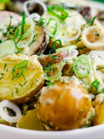 A bowl of creamy potato salad with sliced radishes, green onions, fresh dill, and a fork.