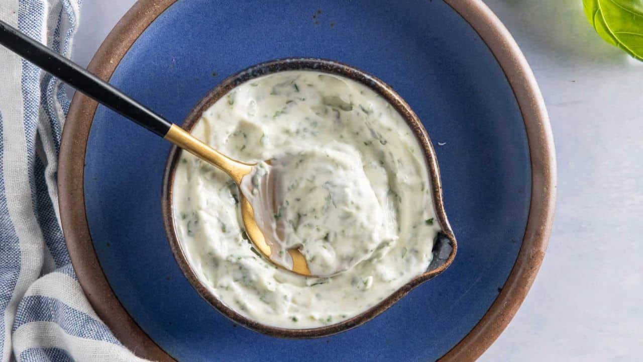 A top-down view of a small bowl filled with basil mayonnaise on a blue plate.