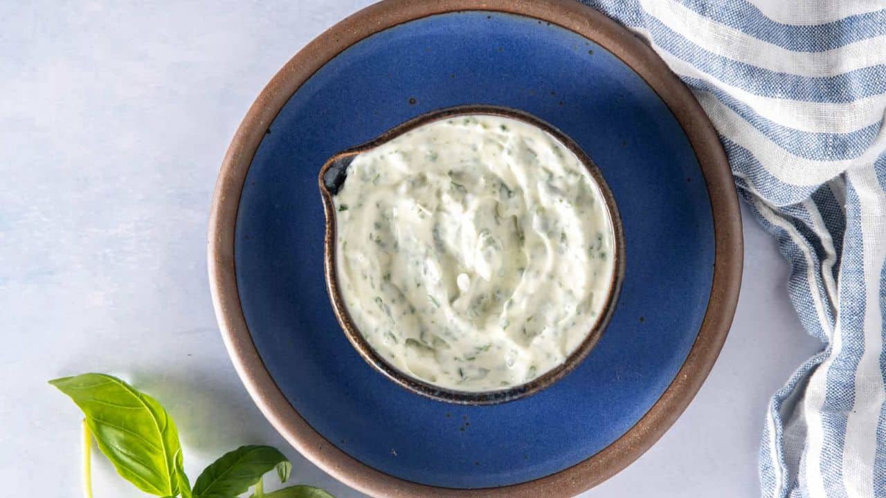 A top-down view of a small bowl filled with basil mayonnaise on a blue plate.