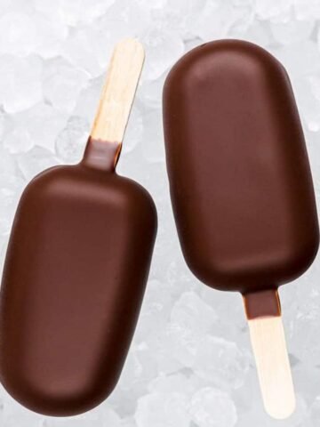 Four chocolate-covered ice cream bars on wooden sticks are arranged on a bed of ice cubes.