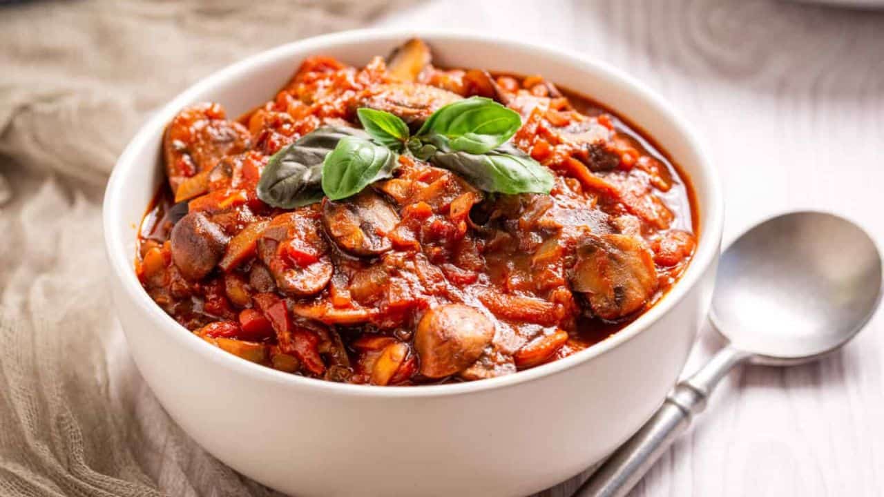 An image of mushroom ragu in a white bowl with a garnish of basil on top.