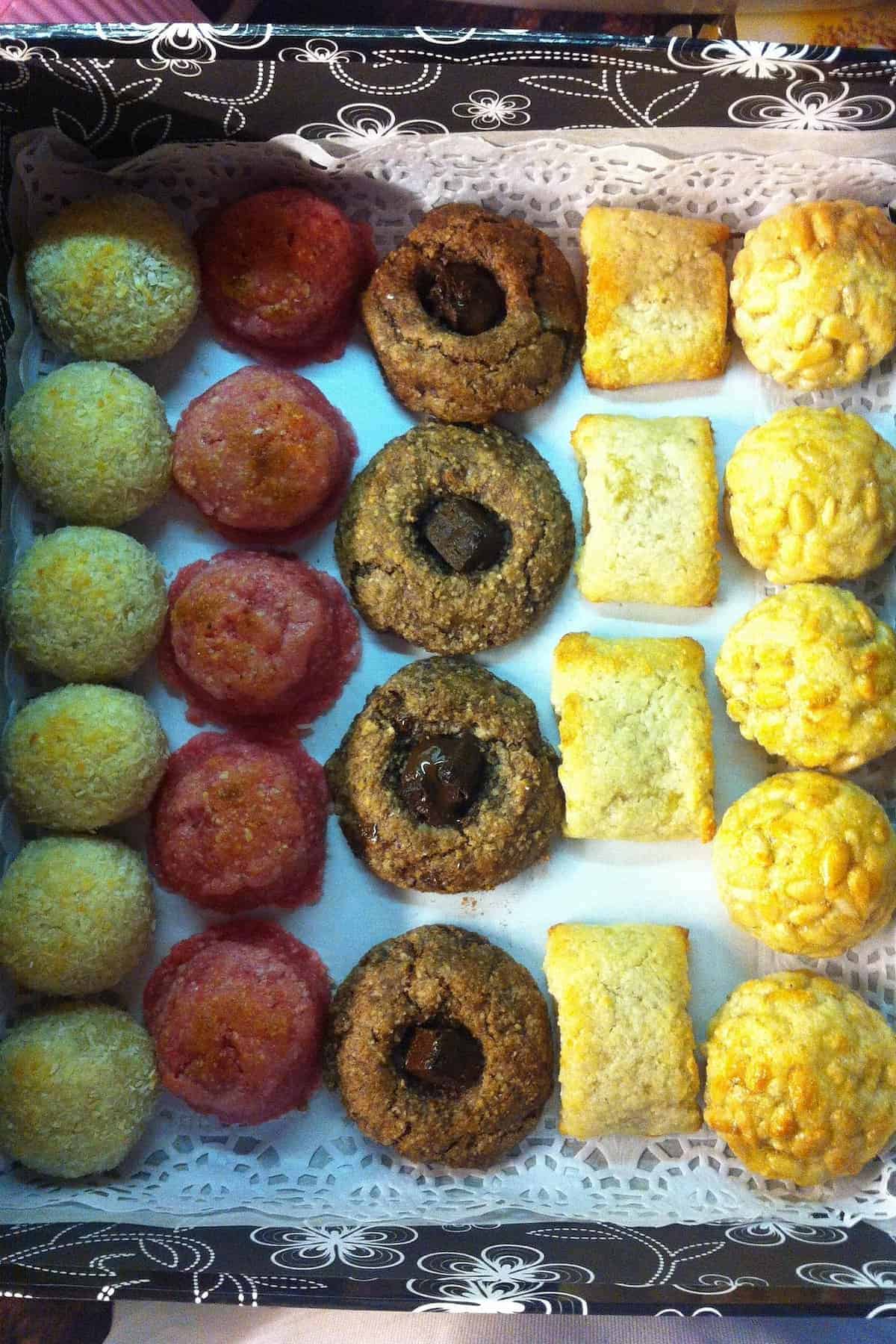 An assortment of colorful cookies arranged neatly in rows inside a decorative box lined with lace paper.