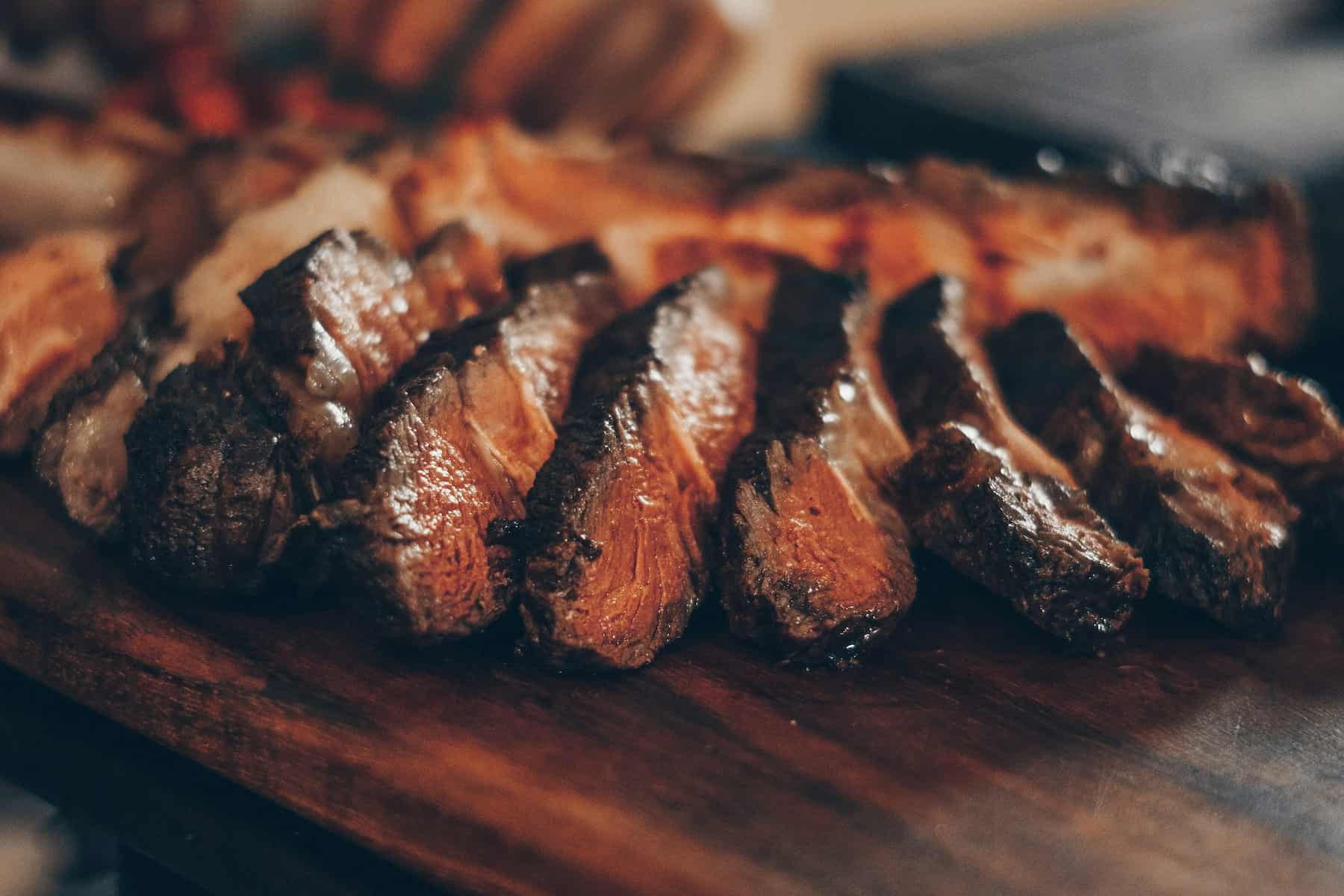 Sliced cooked steak arranged on a wooden cutting board.