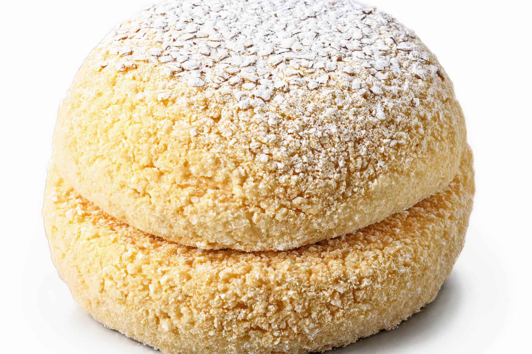 Close-up of a round, golden, crumbly cookie dusted with powdered sugar on a white background.
