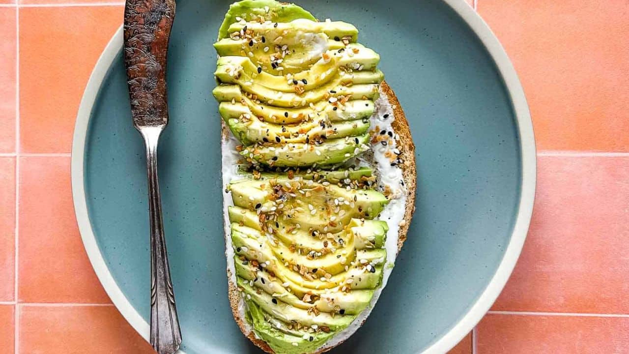 Finished avocado tartine with a vintage knife on a light blue plate on a medium blue background.