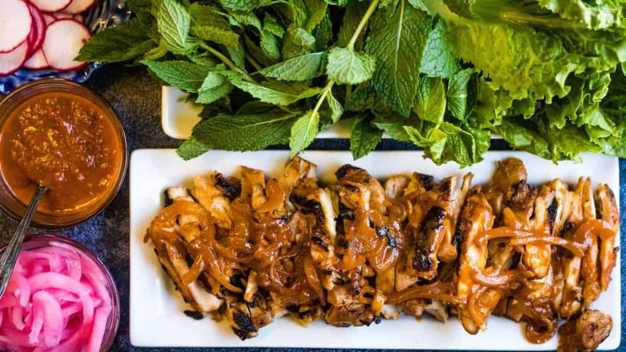 Gochujang chicken on a platter with fresh herbs.