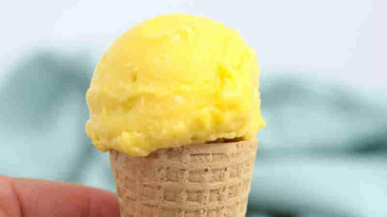 Close up of homemade mango ice cream in a gluten-free cone being held between fingers.