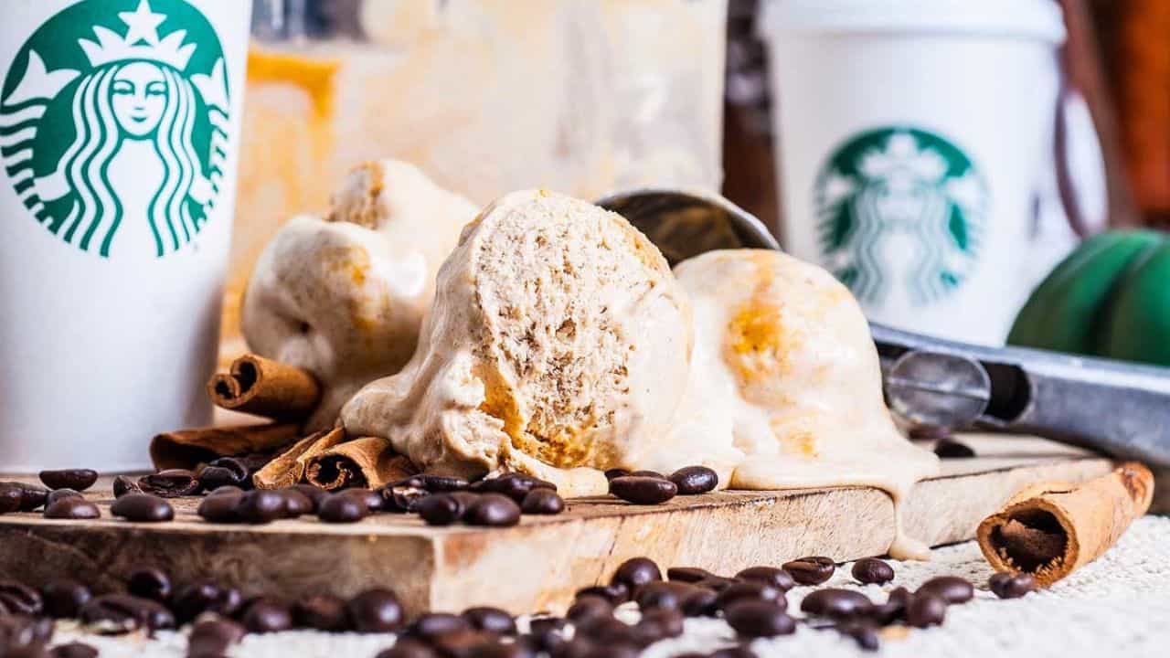 Three scoops of coffee-flavored ice cream on a wooden board with coffee beans, cinnamon sticks, and Starbucks cups in the background.