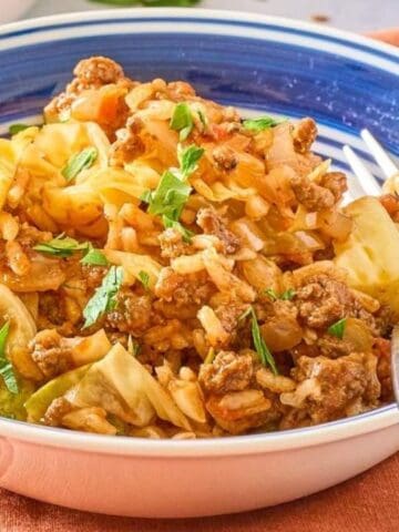 A bowl of cabbage roll casserole with ground meat, rice, chopped cabbage, and herbs, served with a fork on an orange napkin.