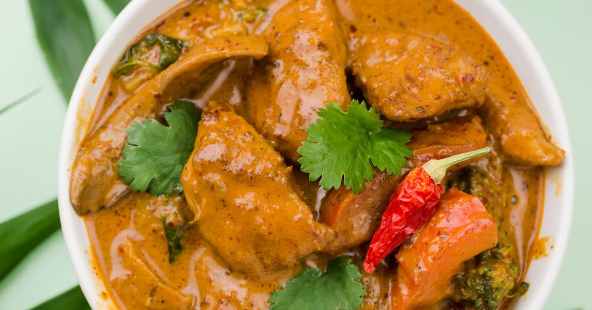 A bowl of Goan food featuring curry with chunks of meat, vegetables, cilantro leaves, and a whole red chili pepper in a creamy sauce.