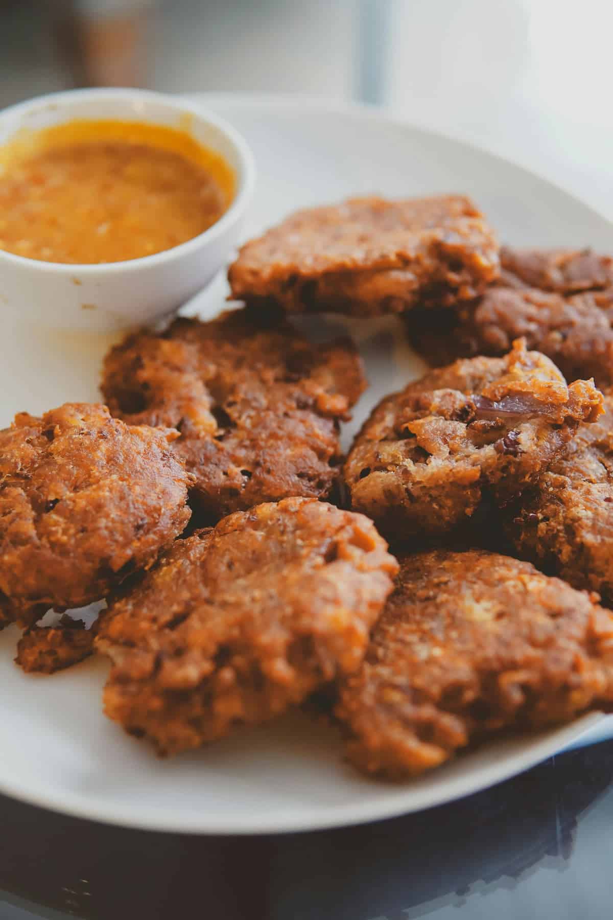 A white plate with several pieces of fried patties and a small bowl of dipping sauce—delightful examples of Bahamas breakfast foods.
