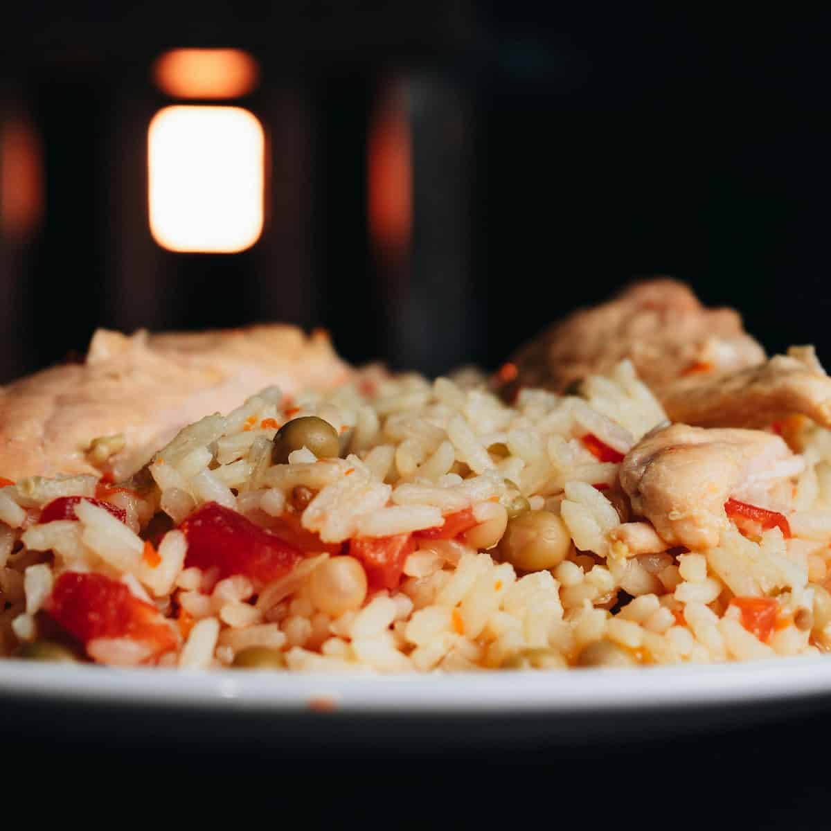 A close-up of a plate of rice mixed with peas, red bell peppers, and pieces of cooked chicken—a flavorful dish inspired by Bahamas breakfast foods—set against a dark background.