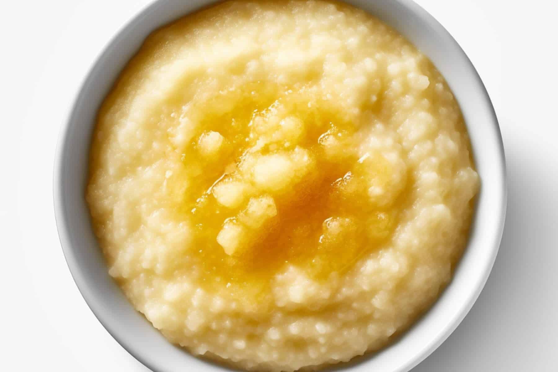 A white bowl filled with creamy grits, a classic among Bahamas breakfast foods, topped with melted butter and viewed from above on a white background.