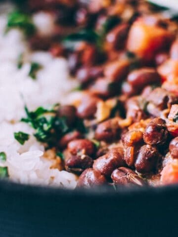 A close-up of a bowl containing white rice, black beans in sauce with chopped herbs, and a lime wedge.